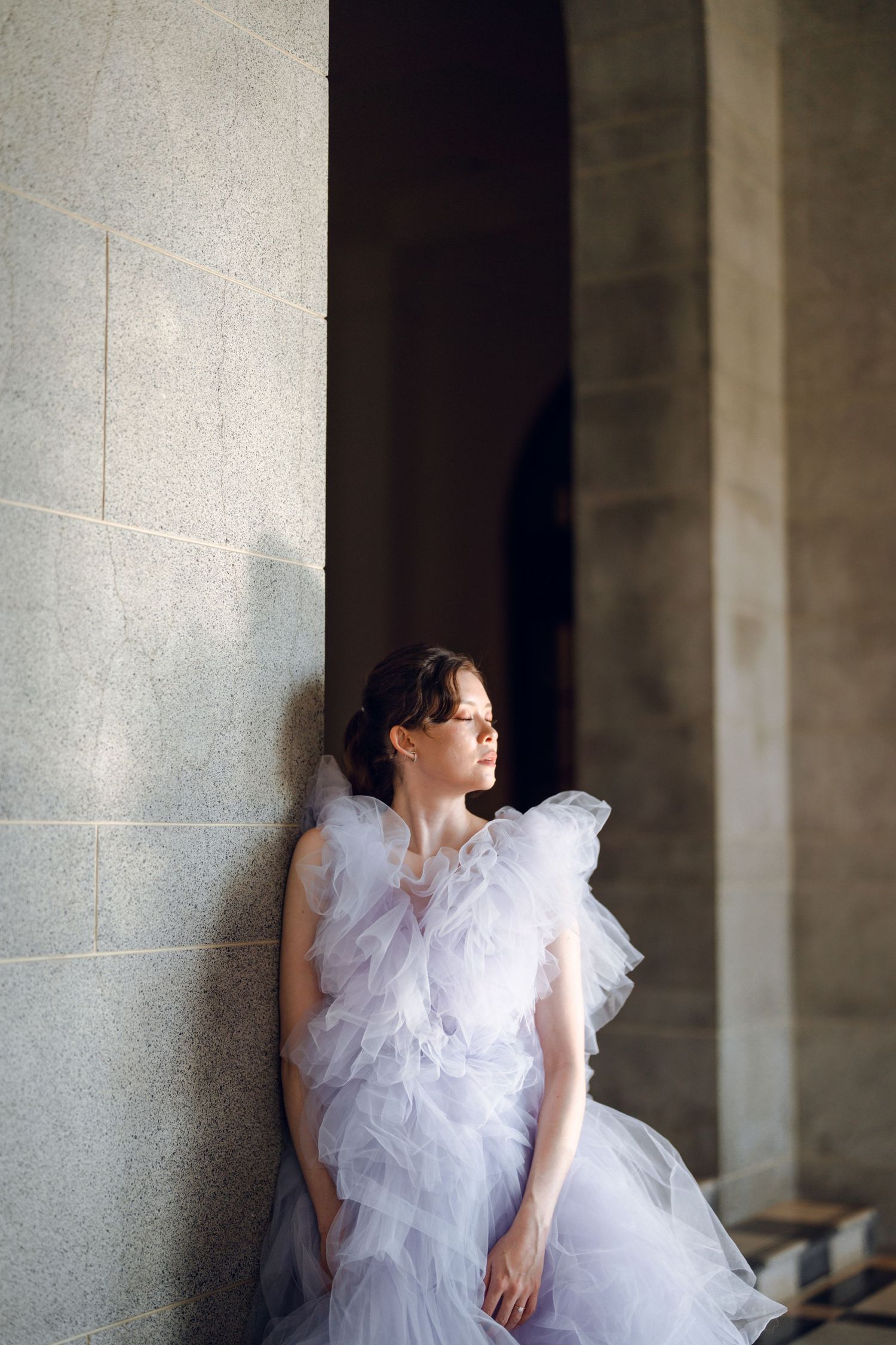 Bride in a flowing lavender tulle gown poses against a stone wall.