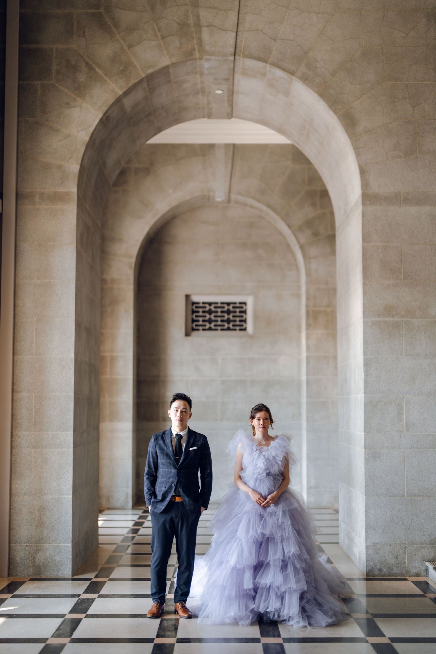 Wedding couple poses formally in an architectural setting with stone arches and natural light.