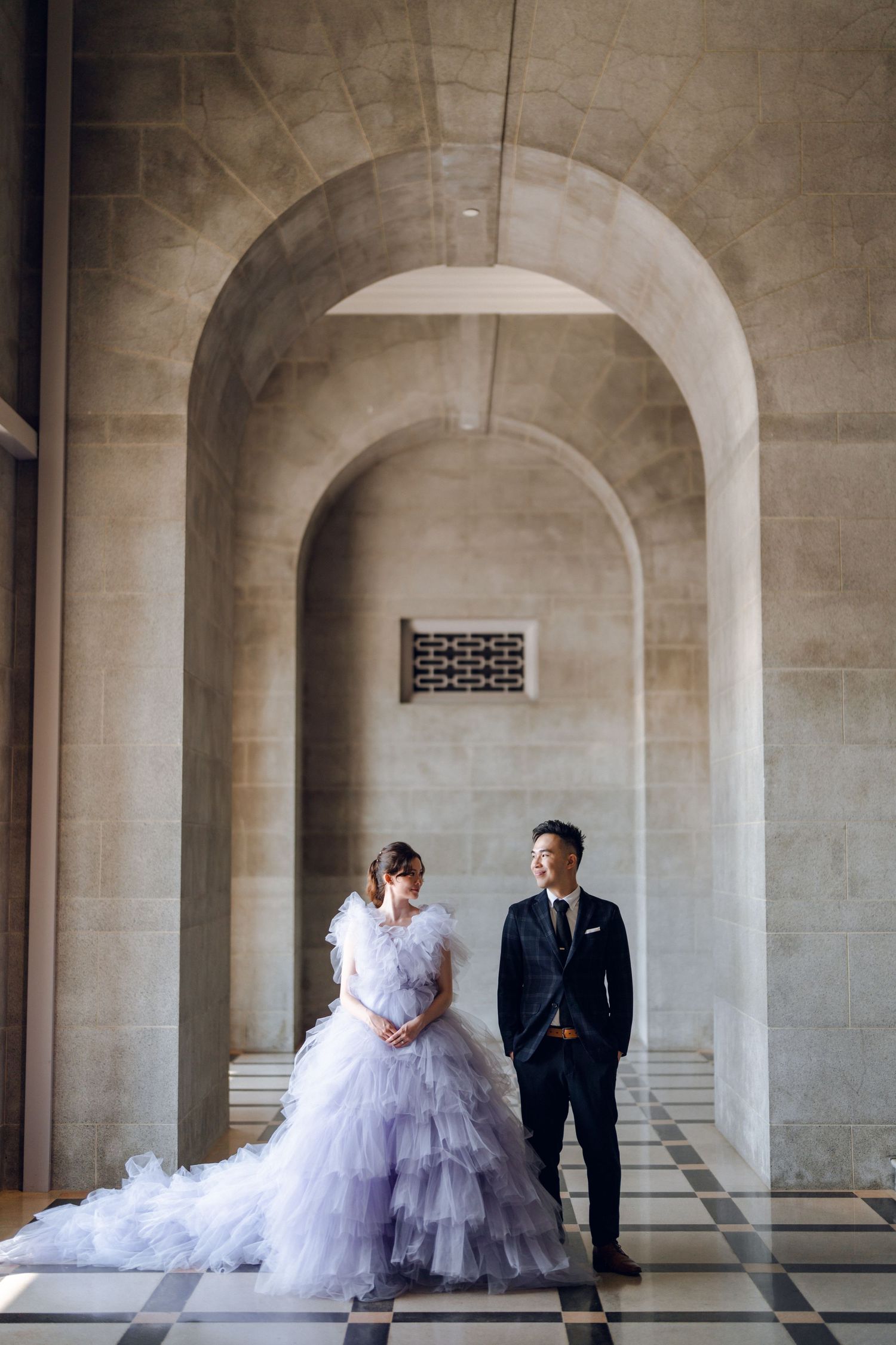 Elegant couple stands beneath stone arches in formal wedding attire.