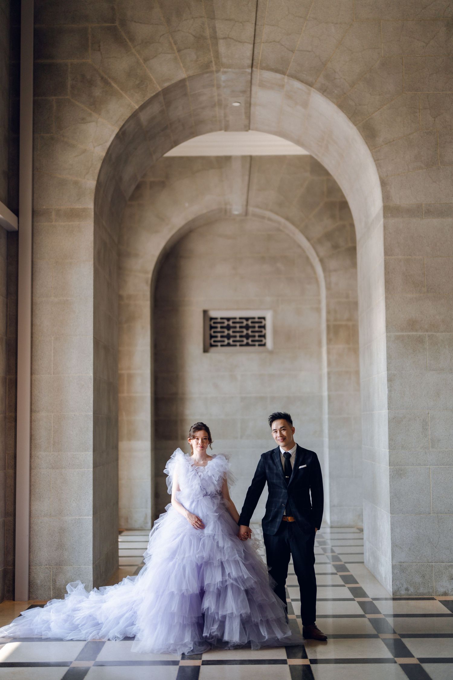 Wedding portrait featuring a couple in formal attire under a grand stone archway.
