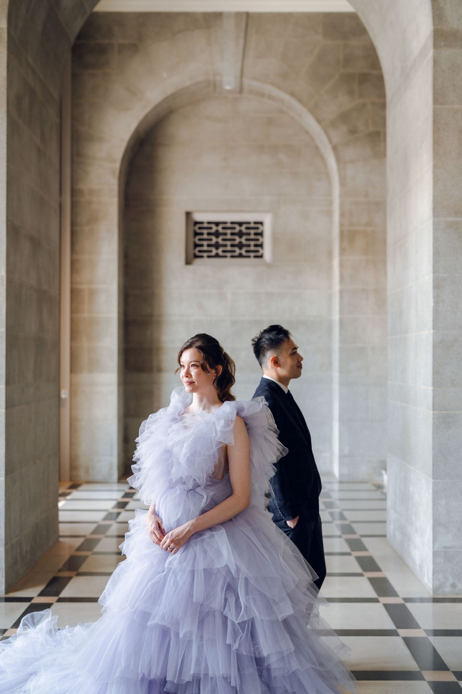 Romantic couple embraces in formal wear under historic stone archways and columns.