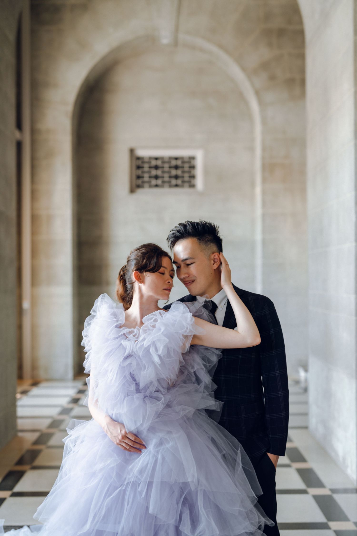 Intimate moment captured between couple in white gown and black suit under stone colonnade.