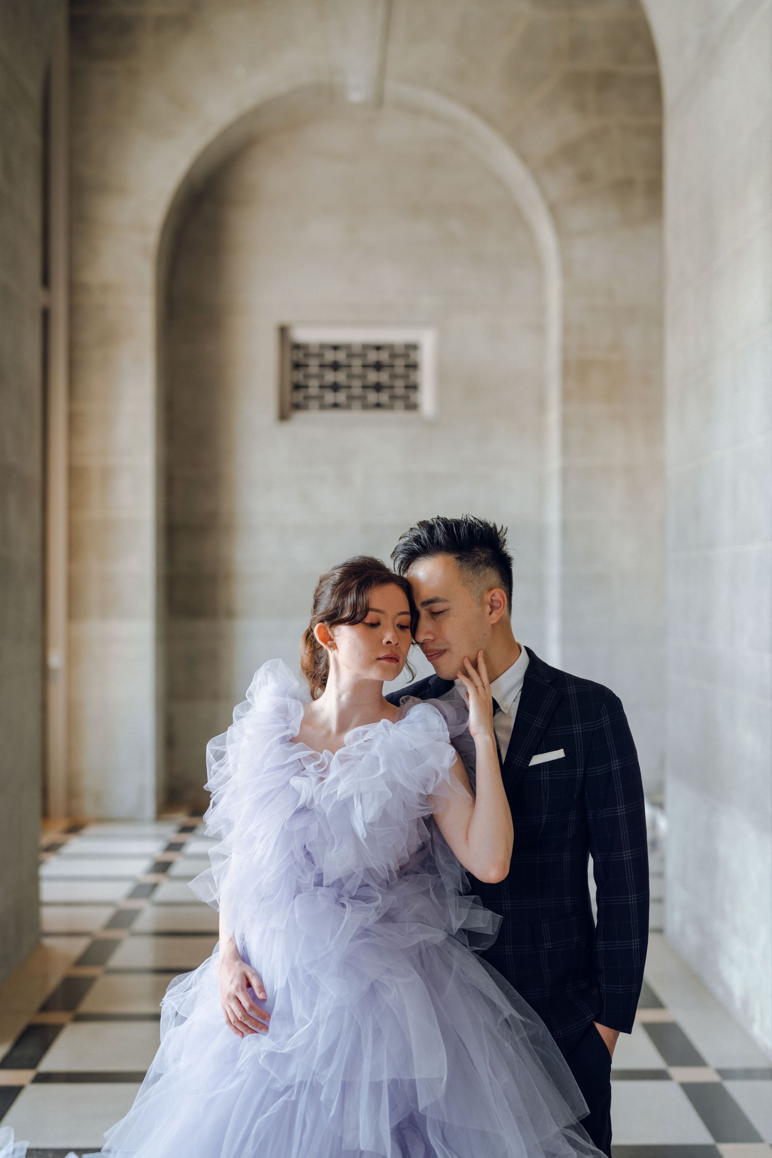 Tender embrace between newlyweds in dramatic stone hallway with arched architecture.