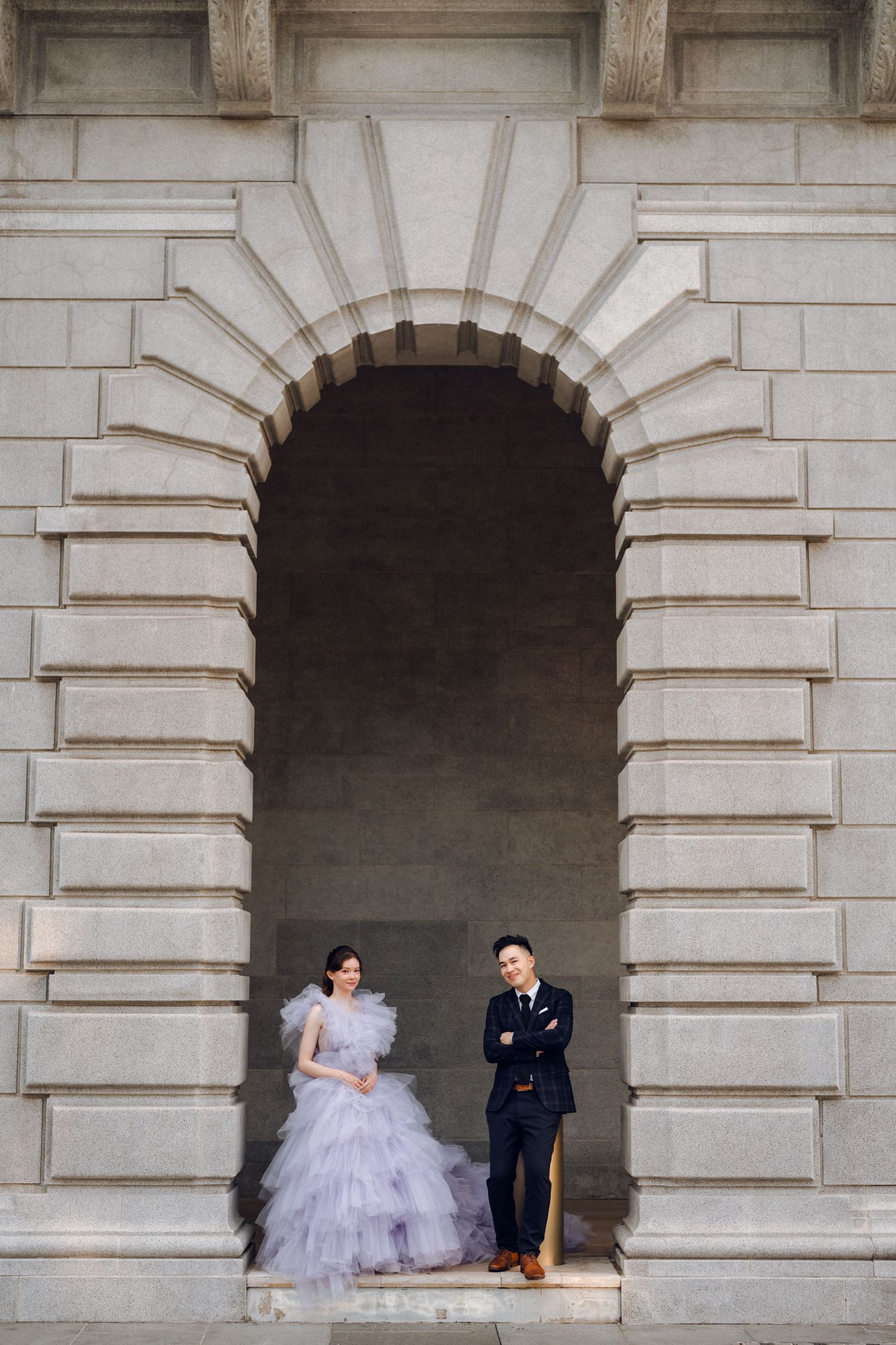 A couple shares a lighthearted moment under a classical stone archway.