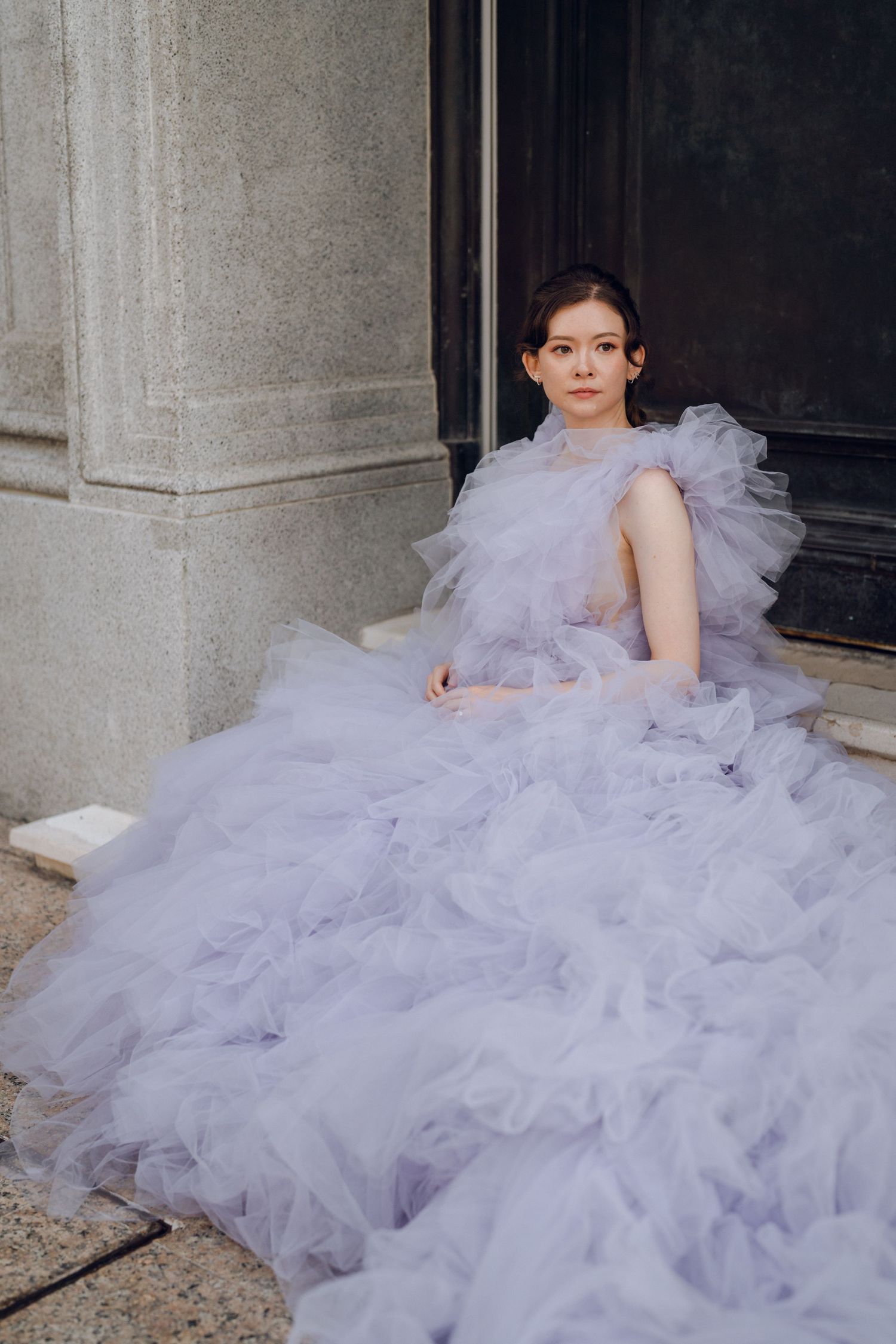 A flowing lavender tulle gown creates a dreamy silhouette against a stone building backdrop.
