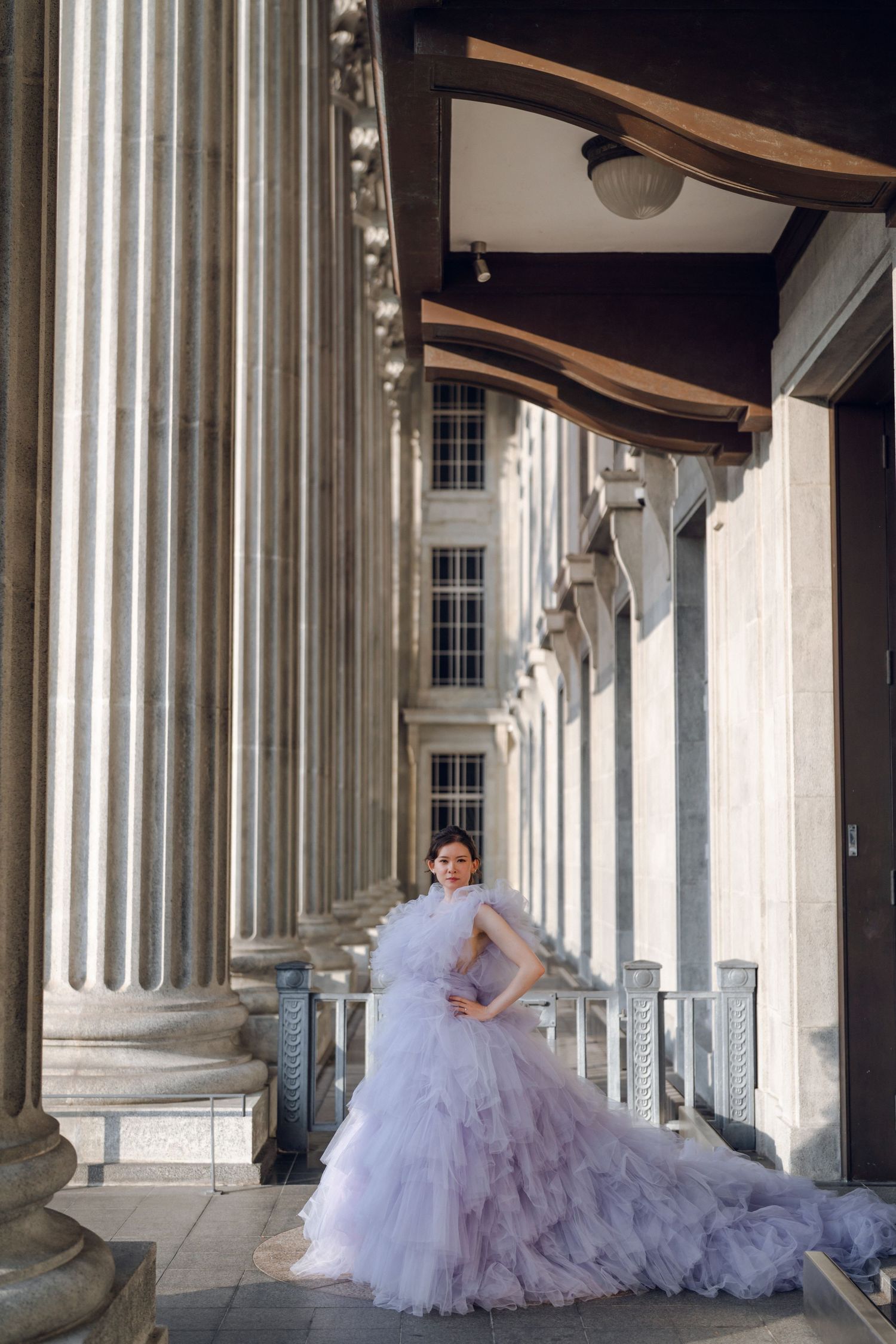 A lavender ball gown creates an ethereal scene among historic stone columns.