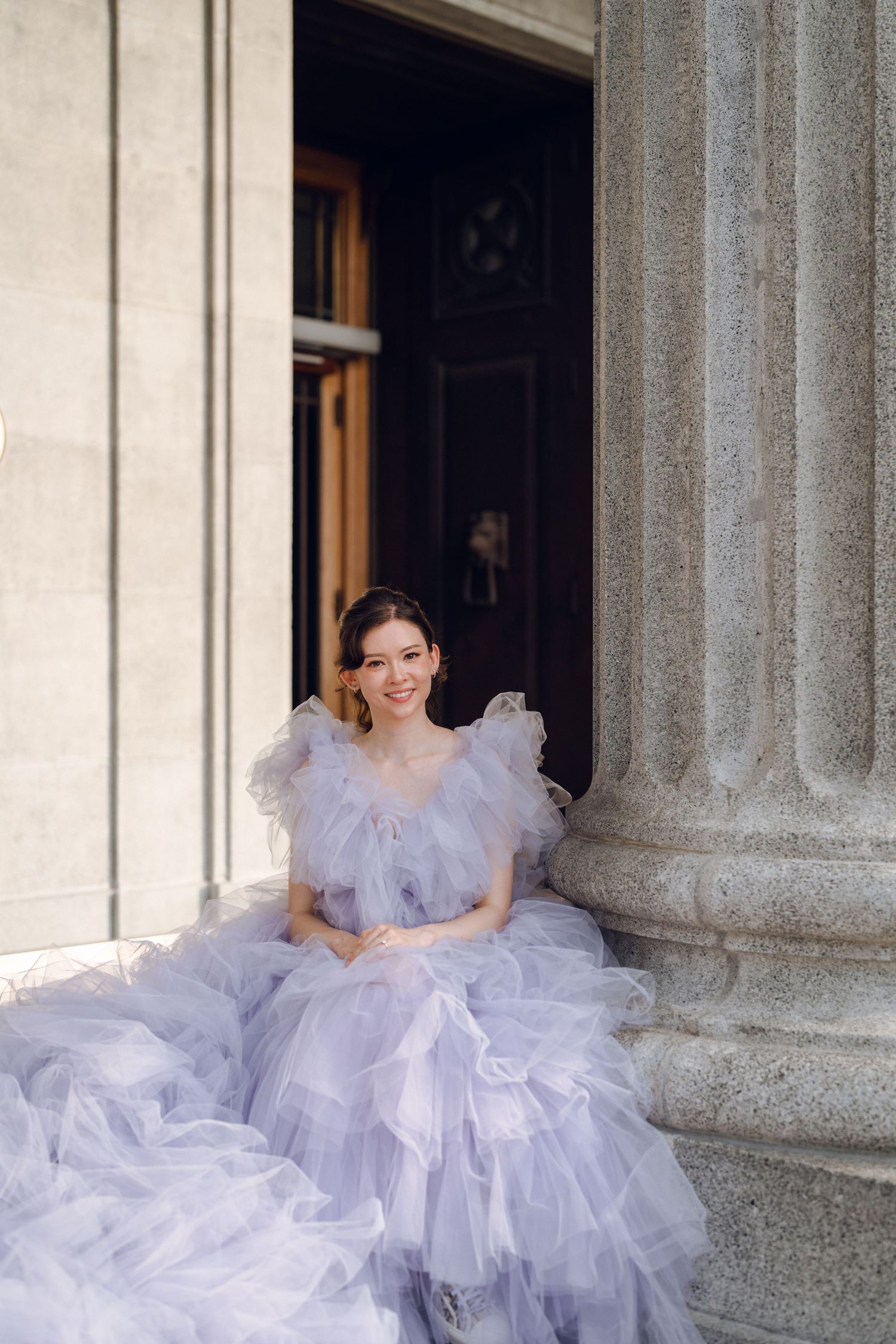 A lavender tulle ball gown creates a romantic scene against classic stone architecture.