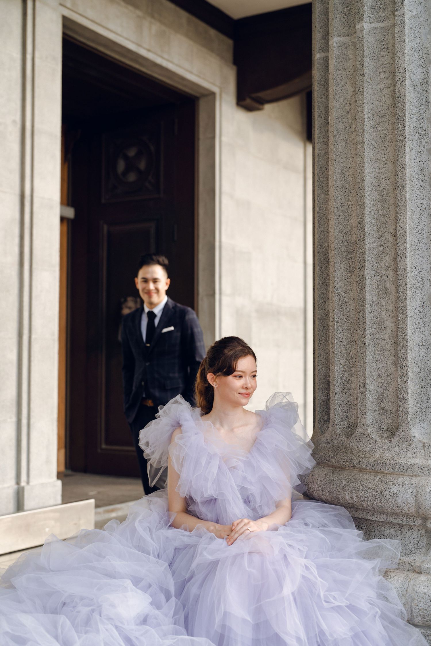 A dreamy lavender gown fills the frame against the backdrop of stone columns.