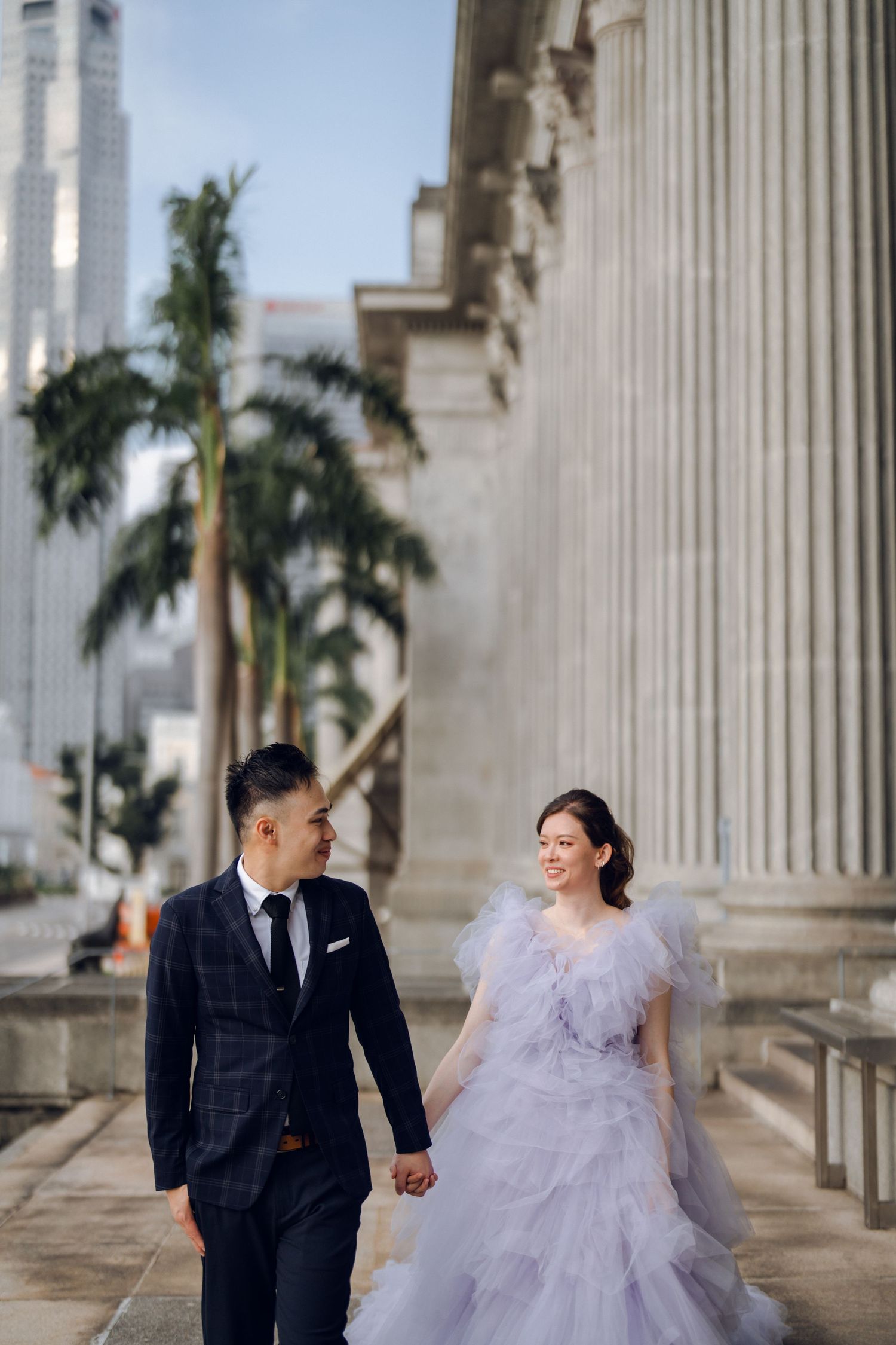 A couple shares a tender moment among classical columns with city skyline visible in background.