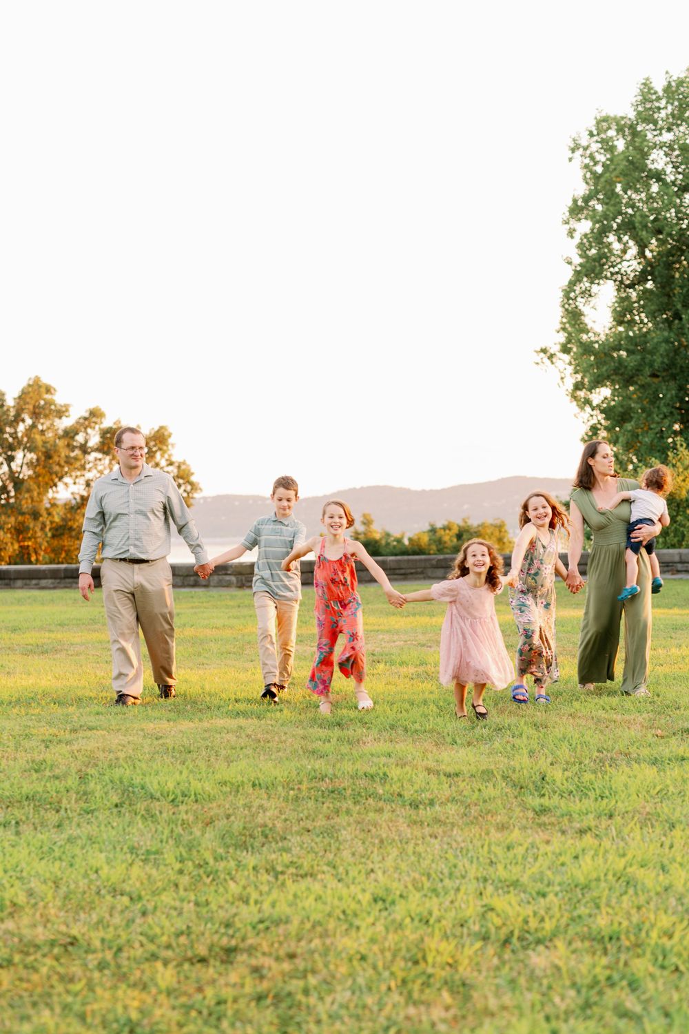 A group walks together holding hands across a grassy field with mountains in the distance.
