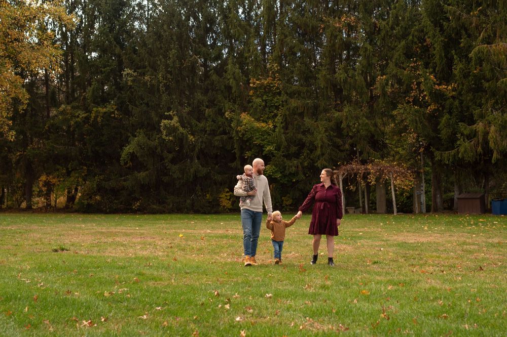People walking together through a scenic fall landscape with trees and grass on a sunny afternoon.