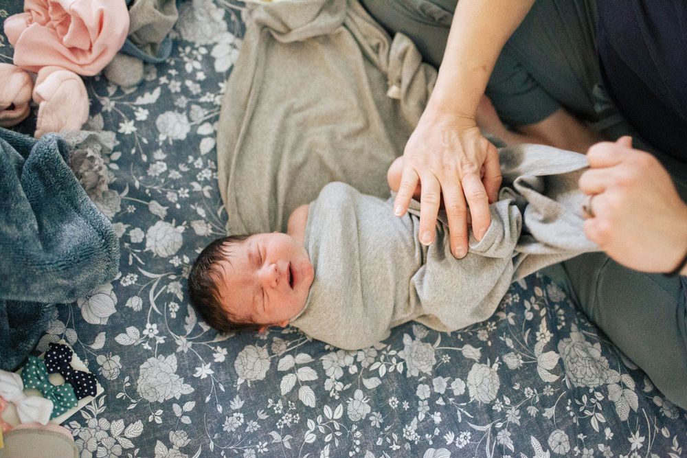 Everett WA fresh 48 photo shoot: A mother swaddles her newborn baby at home during a Fresh 48 Photo shoot