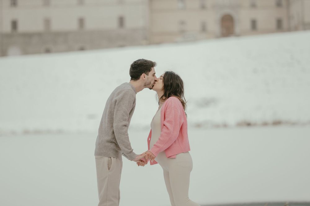 Intimate moment between a couple sharing a tender moment in front of a snowy castle backdrop.