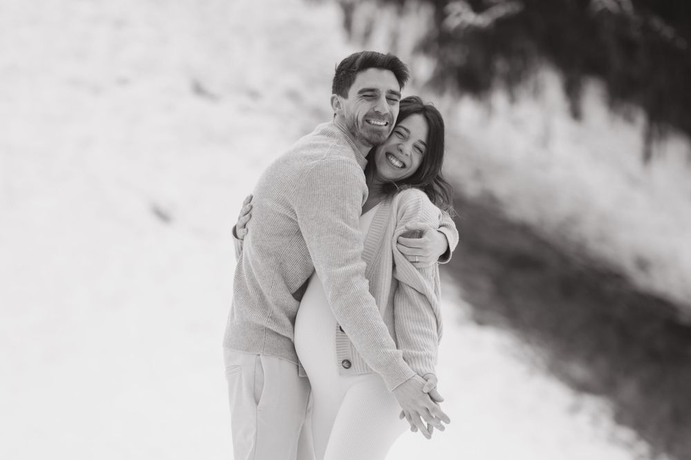 Black and white photograph capturing a couple's tender embrace against a snowy background.