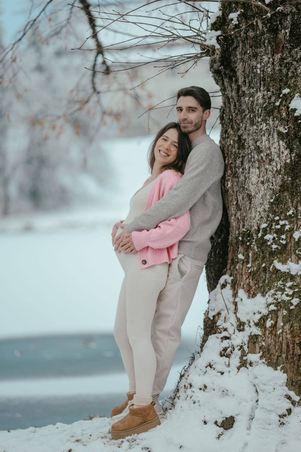 Couple posing against a snow-covered tree in coordinated winter outfits during a photo session.