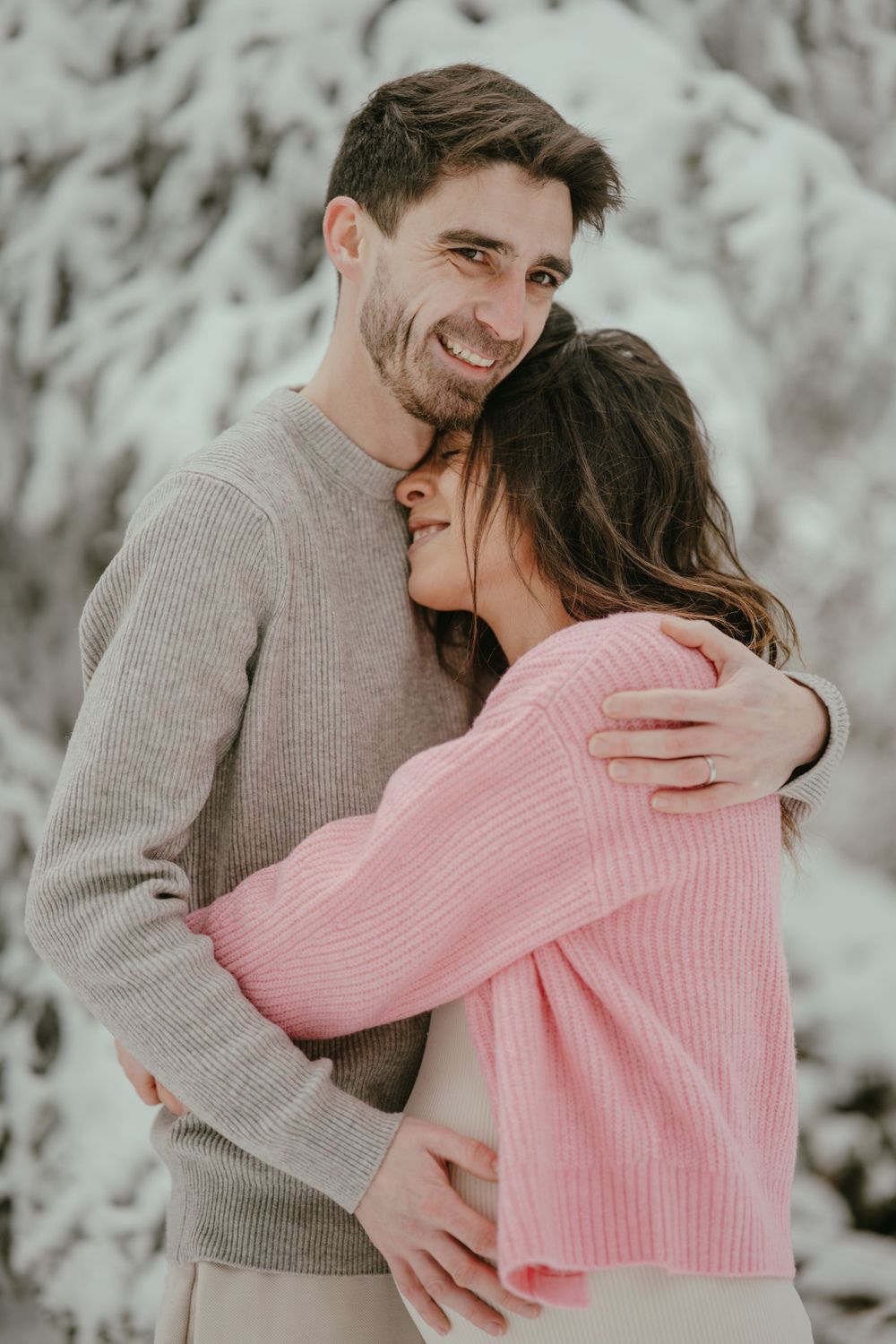 A couple shares an intimate embrace in the snow wearing matching knit sweaters.