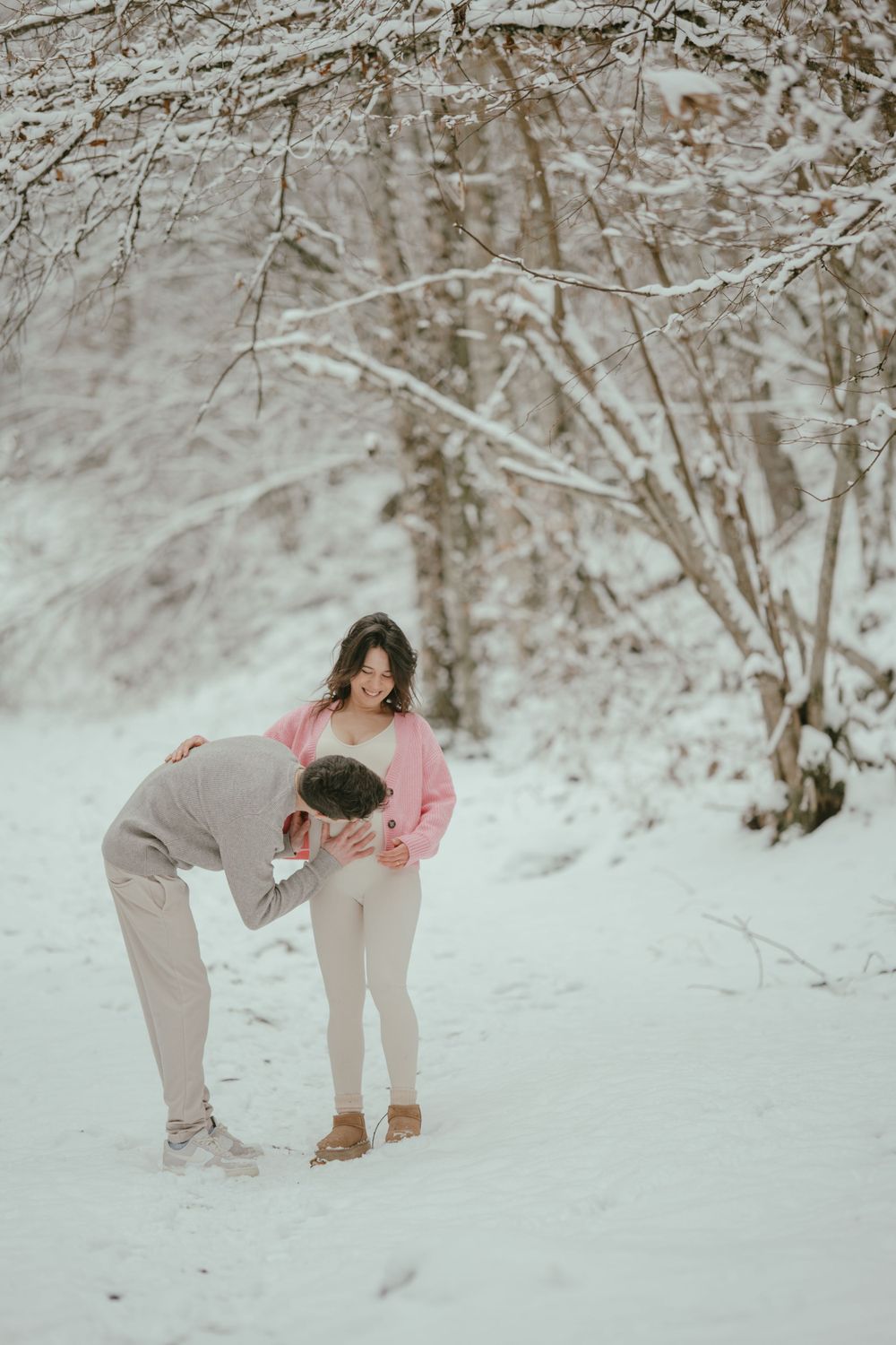 A couple shares a playful moment in a snowy forest setting.