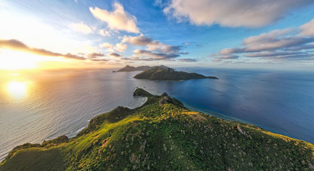 Dramatic sunset view over green coastal cliffs and small islands in the ocean.