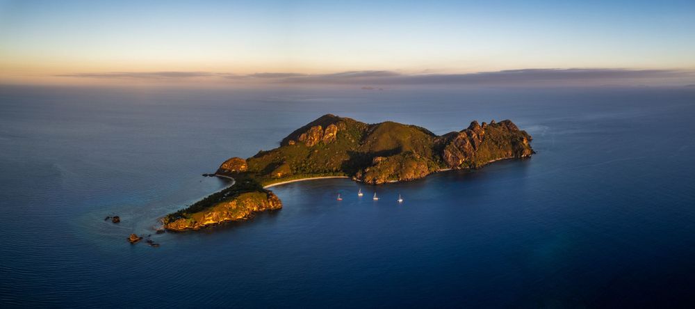 Aerial panoramic view of a rugged tropical island surrounded by deep blue ocean waters at sunset.