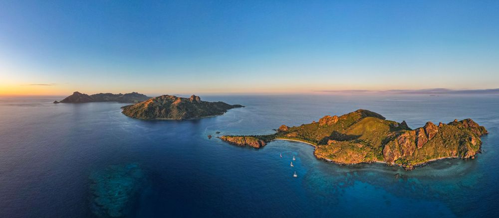 Scenic island archipelago with rocky outcrops and boats anchored in turquoise waters during golden hour.