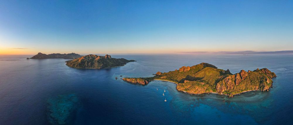 Aerial panoramic view of tropical islands with turquoise waters and rugged coastlines at sunset in calm ocean.