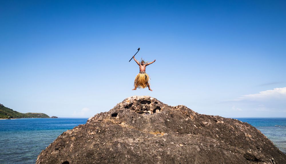 Silhouette of person celebrating on coastal rock formation against ocean backdrop.