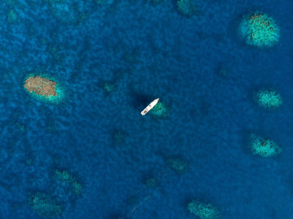 Aerial view of boat surrounded by coral reefs in crystal clear blue waters.