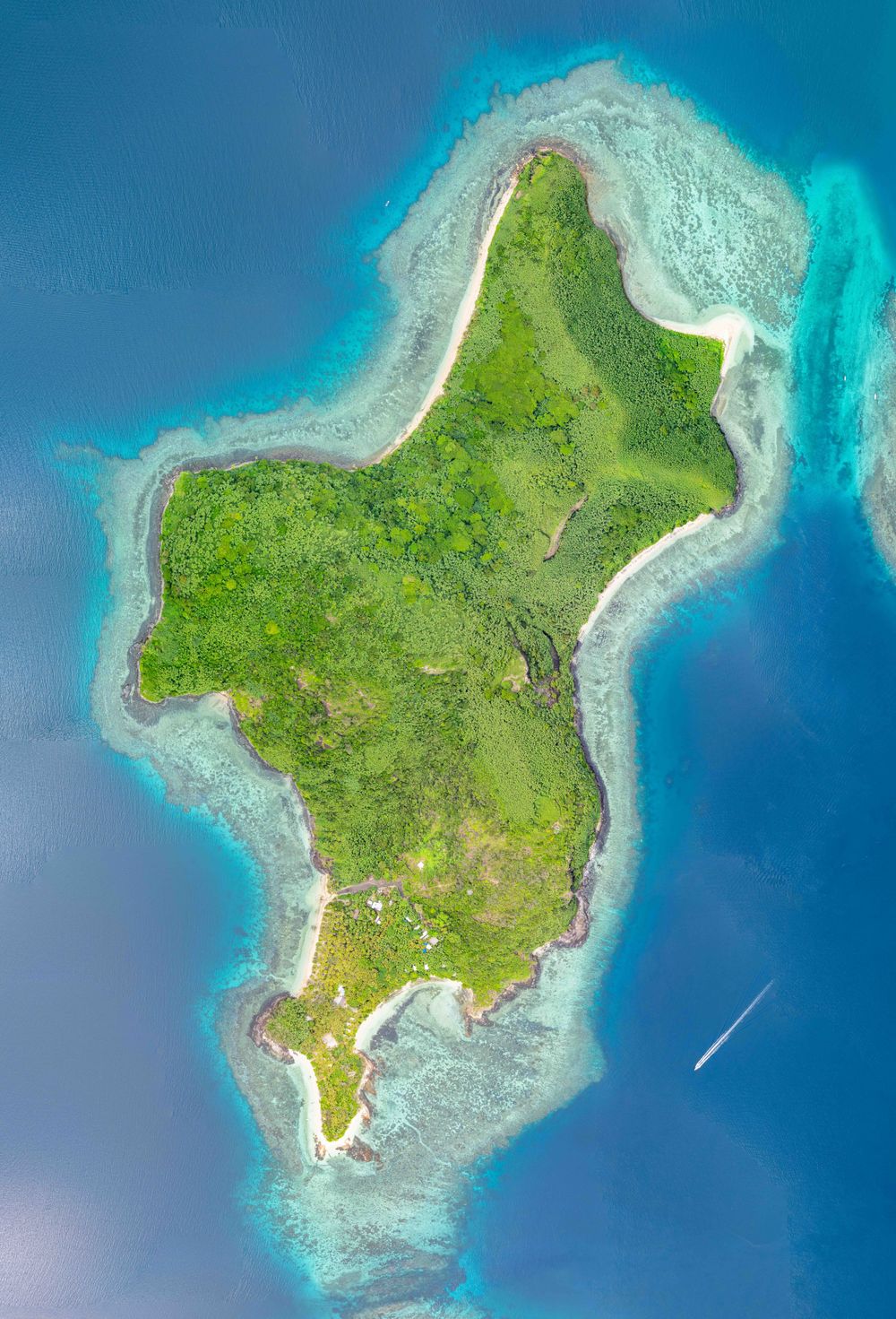 Aerial view of a tropical island with lush green vegetation surrounded by bright turquoise coral reefs and blue ocean waters.