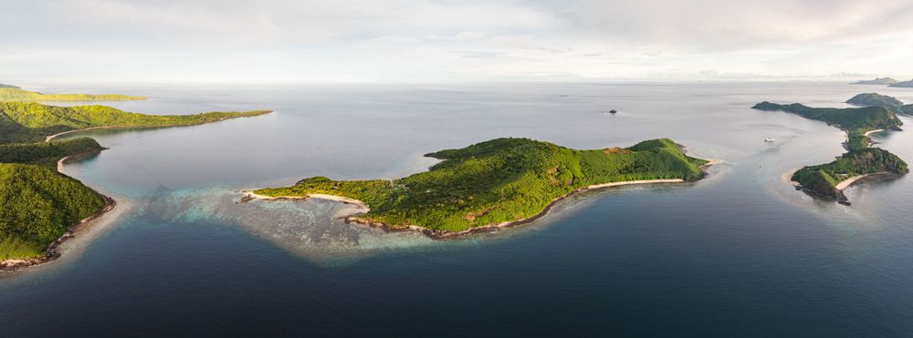 Panoramic aerial view of green islands dotting a calm blue ocean bay under cloudy skies.