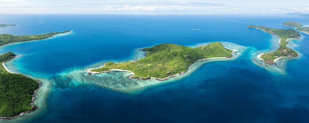 Aerial panorama of a tropical Caribbean island with turquoise waters and lush green vegetation surrounded by coral reefs.