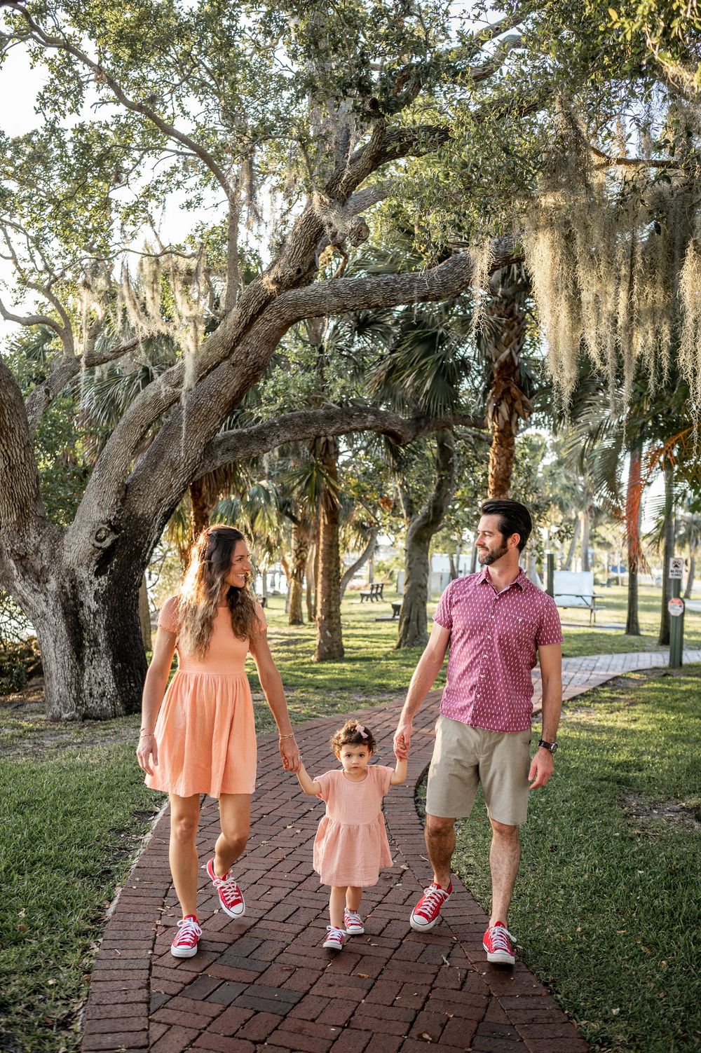 Family portrait featuring a mother, father, and a child holding hands trees park Palm Bay Melbourne Cocoa Beach Vero Florida Brevard County