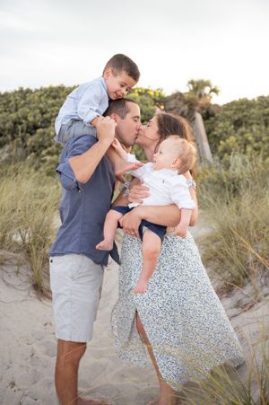 Family portrait photoshoot featuring a kissing mother, father, and two kids standing together on a beach Melbourne Cocoa Beach Vero  Florida