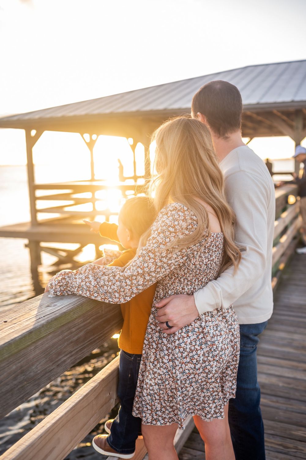 Family portrait featuring a mother, father, and a child standing together on a pier at sunset looking over water candid Melbourne Florida