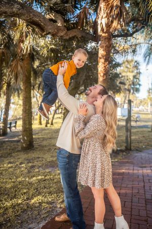 Family portrait featuring a mother, father, and a child dad holding trees park Palm Bay Melbourne Cocoa Beach Vero Florida Brevard County