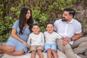 Family portrait featuring a smiling mother, father, and two kids sitting together on beach Palm Bay Melbourne Cocoa Beach Vero Beach Florida