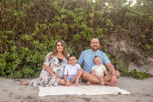 Family portrait featuring a smiling mother, father, and two kids sitting together on beach Palm Bay Melbourne Cocoa Beach Vero Beach Florida