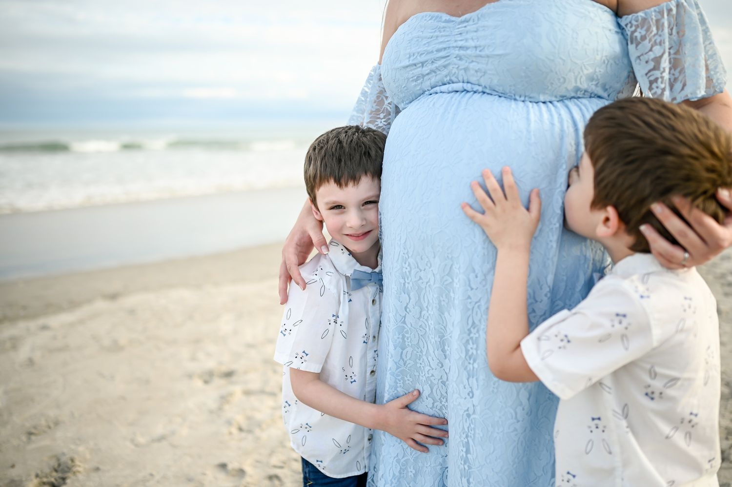 Two little kids at maternity session photoshoot kissing mothers pregnant belly on beach sunset Melbourne Cocoa Vero Florida Brevard County