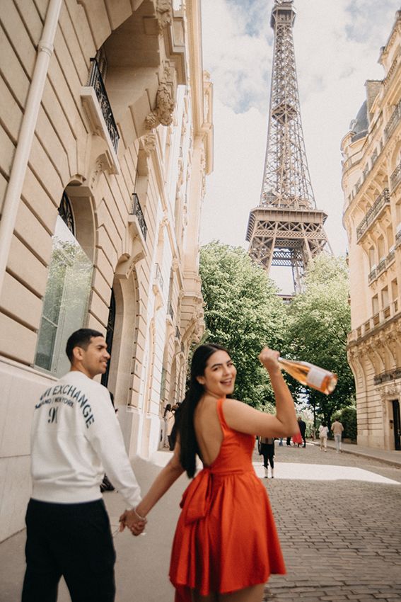 Couple holding hands on a cobblestone street in Paris with the Eiffel Tower visible in the background.