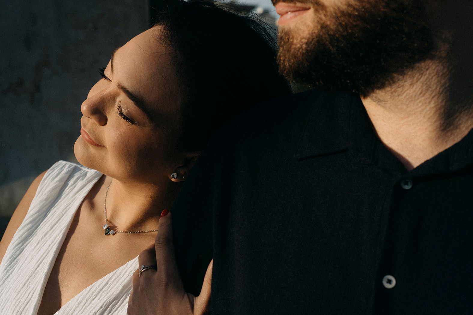 Intimate couple portrait with soft sunlight, woman with closed eyes leaning on bearded man's shoulder.