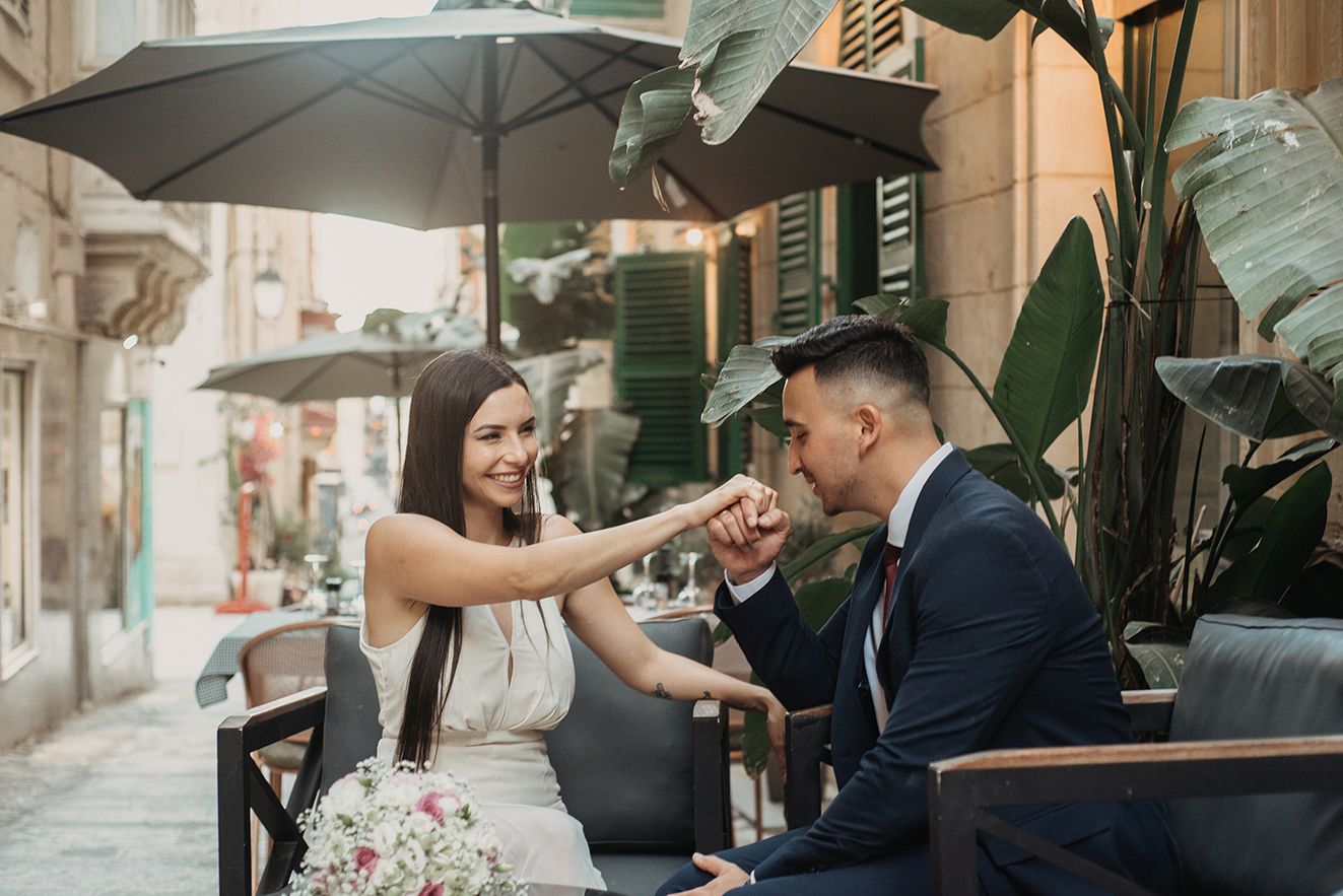 Bride and groom sharing a tender hand-kiss moment at an outdoor cafe in a charming alley.