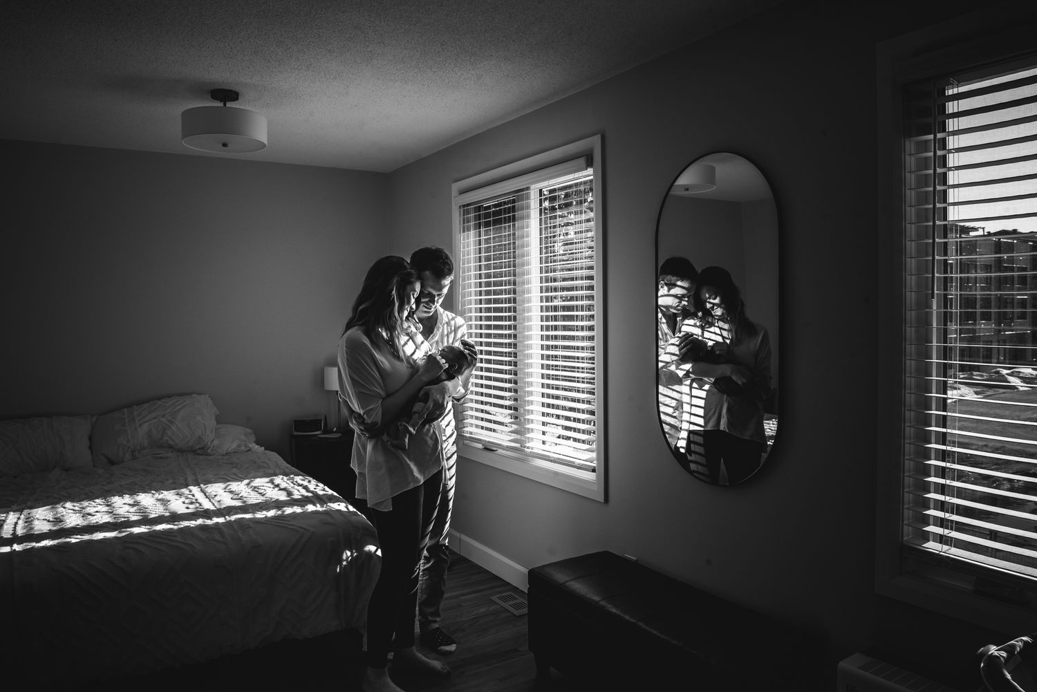 BW image of a couple holding their newborn reflected in their bedroom mirror.