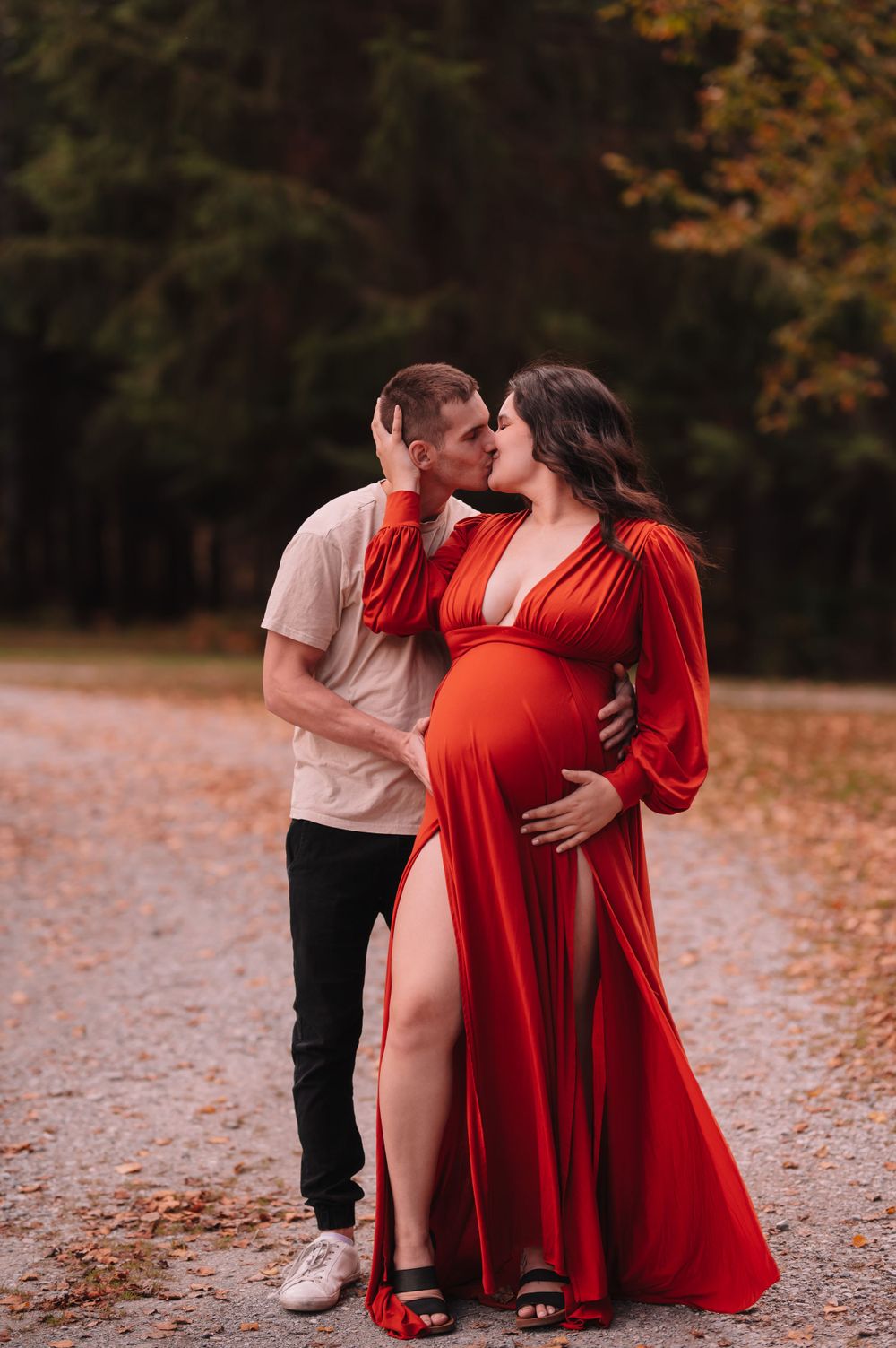 Romantic maternity photo of couple embracing on autumn path with red dress.