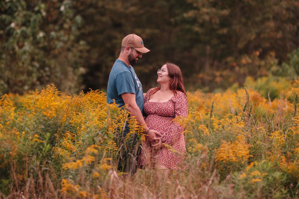 Couple stands together in a field of yellow wildflowers during a romantic maternity photoshoot.