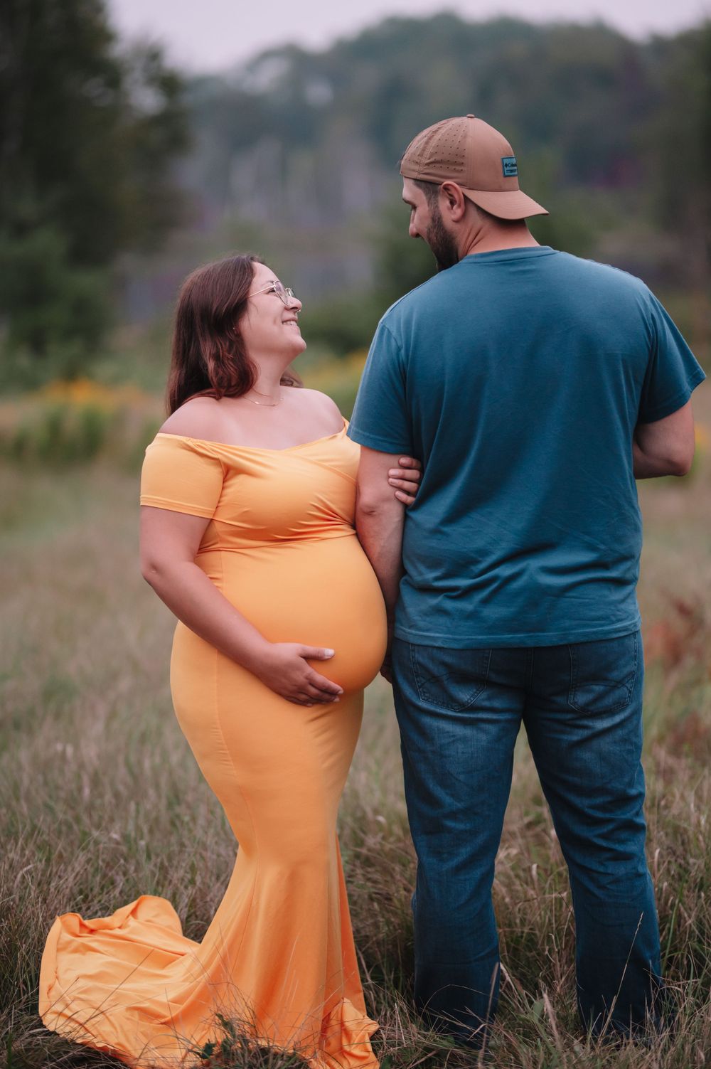 Expectant couple shares an intimate moment in a field, with the mother wearing a flowing orange dress.
