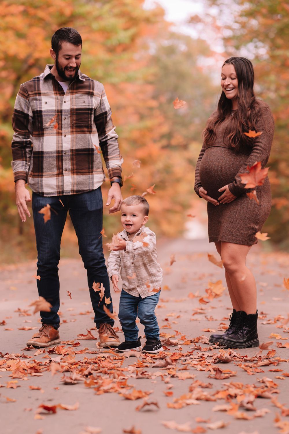 Family walks together on path covered in fallen autumn leaves.