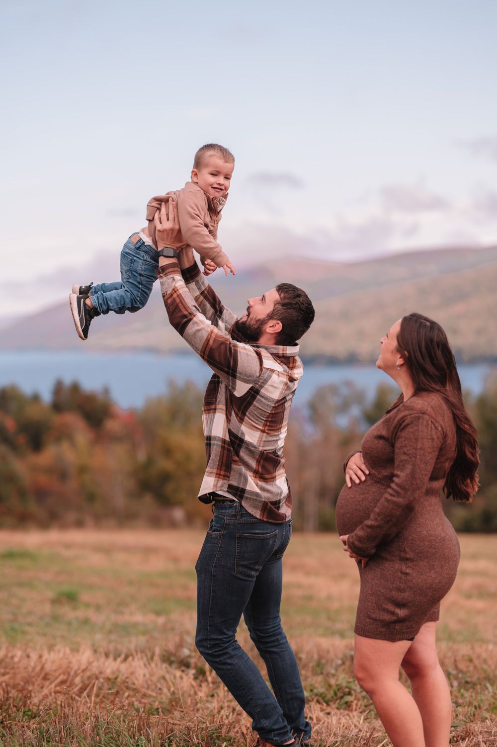 Family enjoys playful moment outdoors with mountains and autumn scenery in the background.