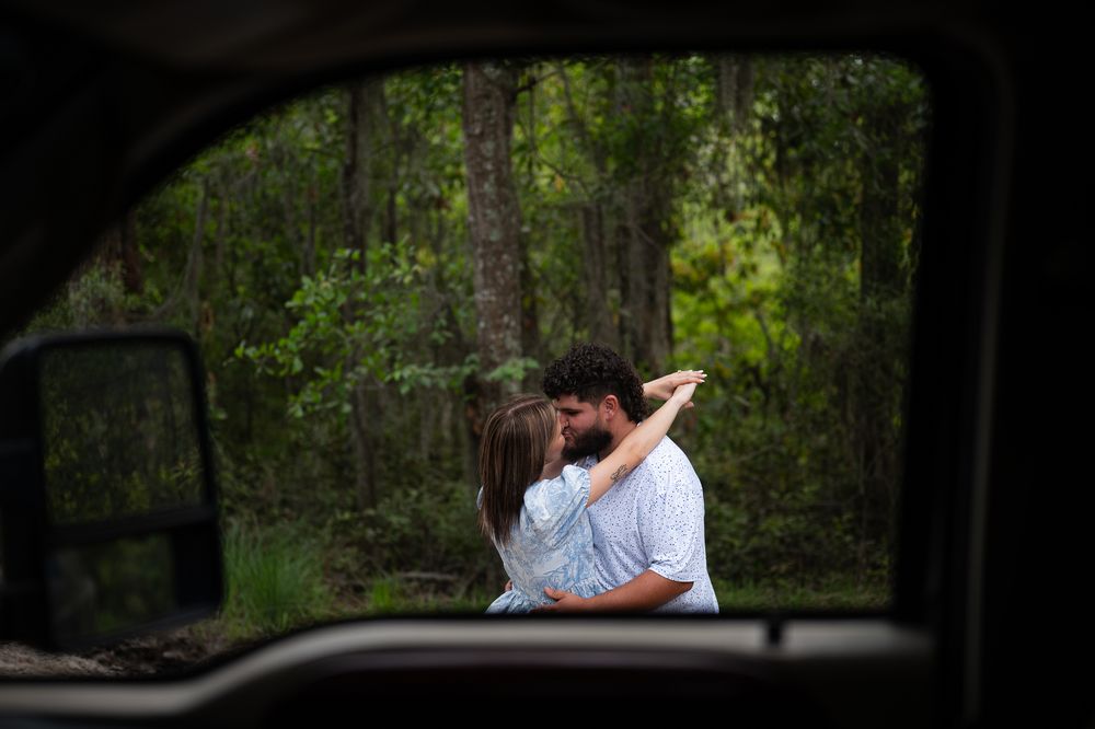 Couple embracing in a romantic forest photoshoot with sunlight filtering through the trees.