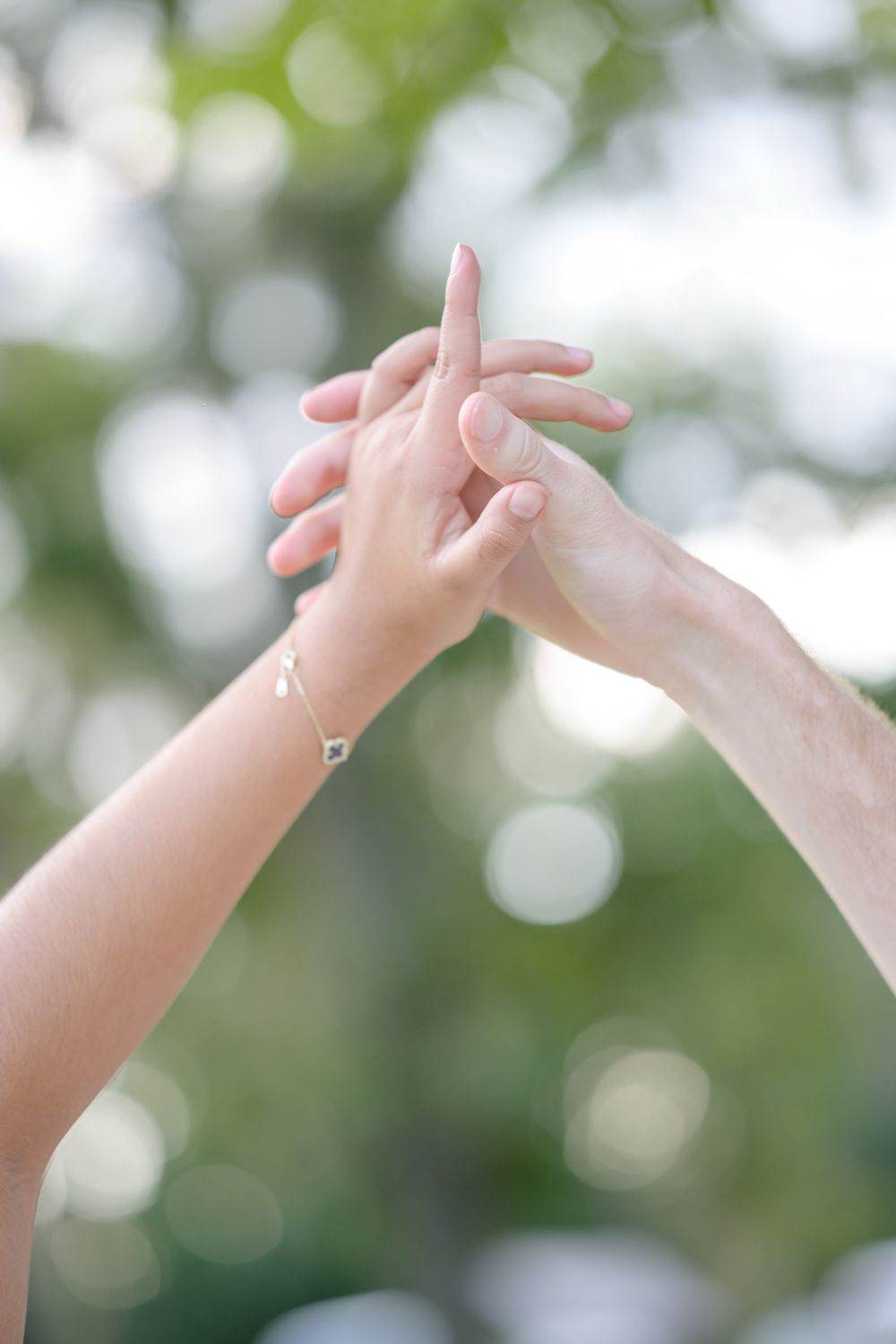 Two hands reaching towards each other against a soft bokeh background.