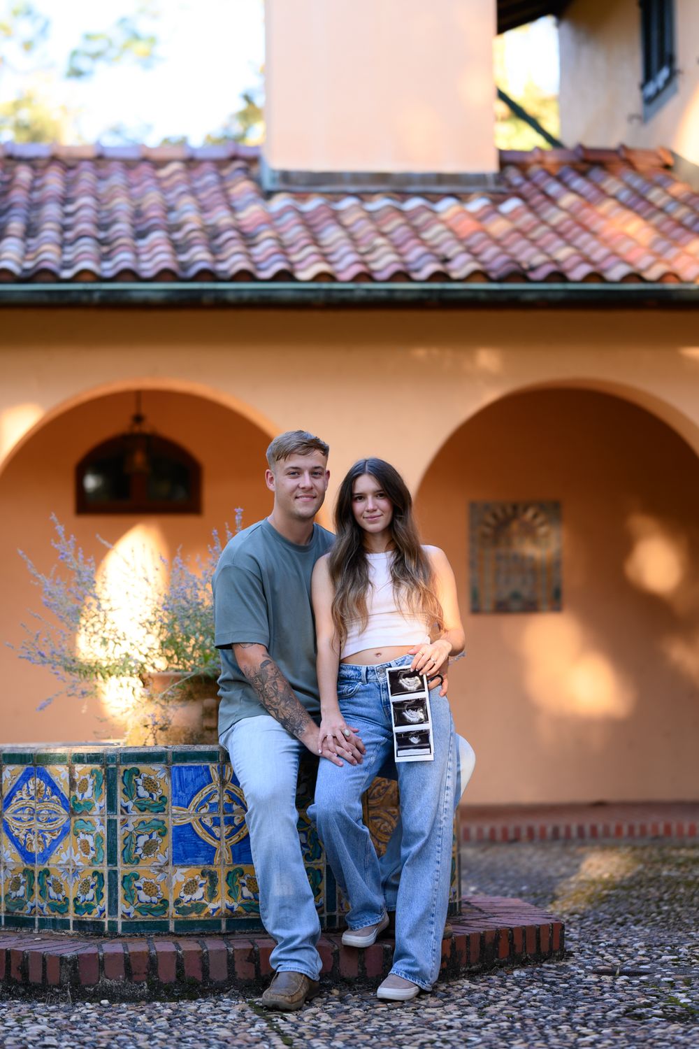 Couple sitting on decorative tile bench against Spanish-style stucco building.