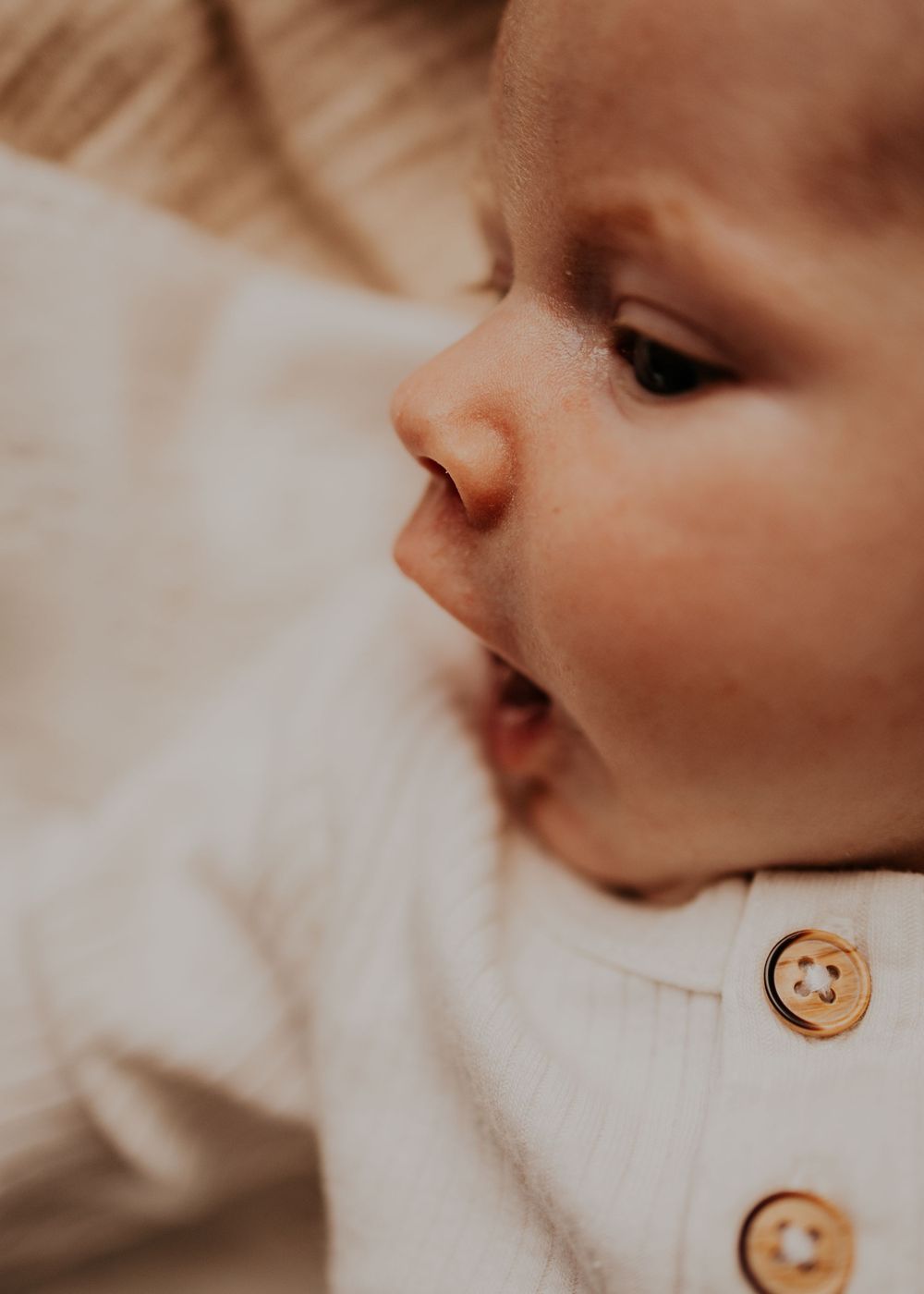 Close-up of a baby's face showing wooden buttons on white clothing.